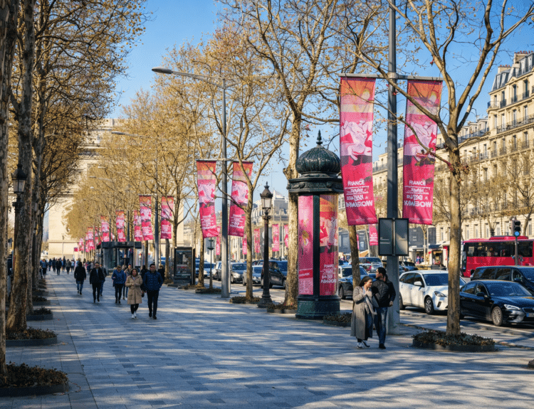 Avenue des Champs-Élysées à Paris avec des piétons marchant sur un large trottoir bordé d’arbres et de bannières, sous un ciel bleu.