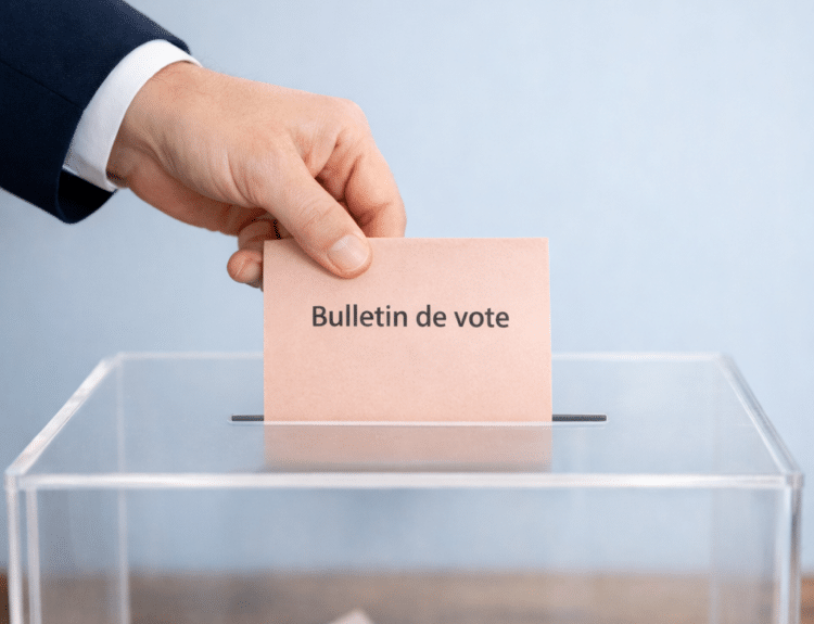 Main déposant un bulletin de vote dans une urne transparente